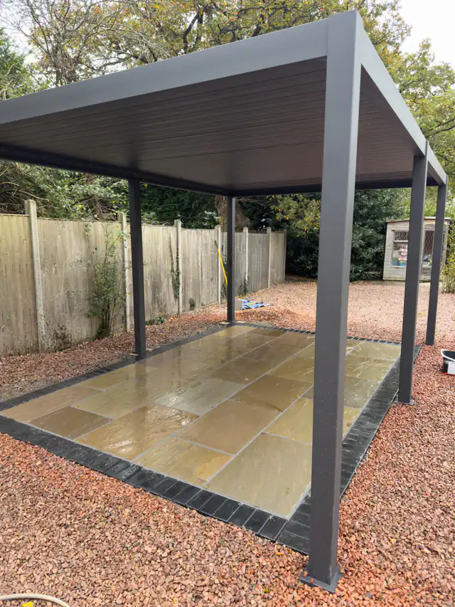 Stone patio with a dark border beneath a garden pergola