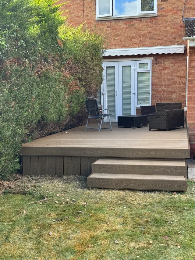 Raised composite deck and steps with light-brown wood-grain finish, installed against a brick property.